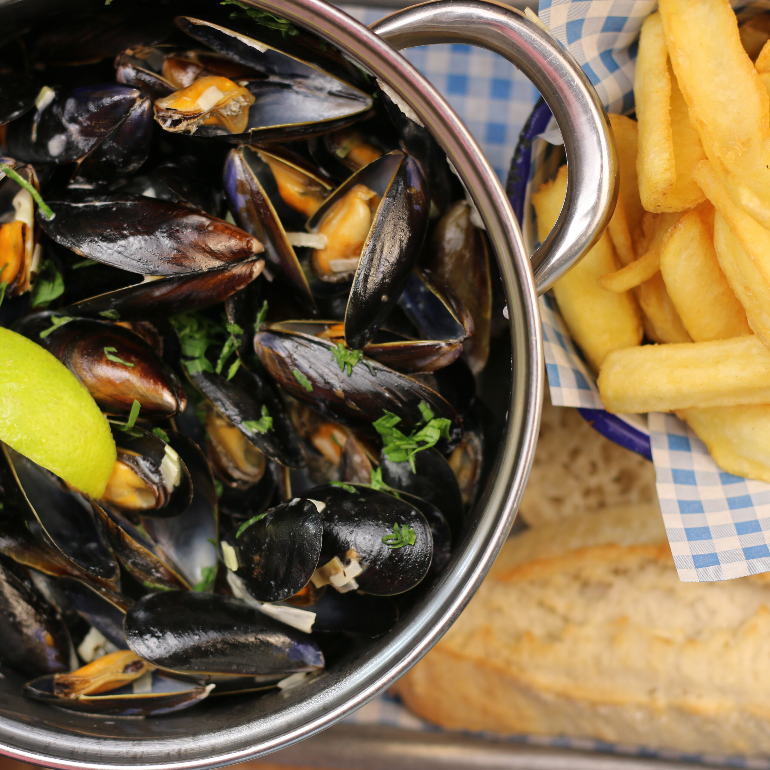 Mussels served in a bowl with a bowl of fries and crusty bread